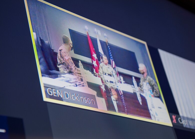 Picture of t.v. screen with video teleconference shot showing three military personnel sitting at a conference table.