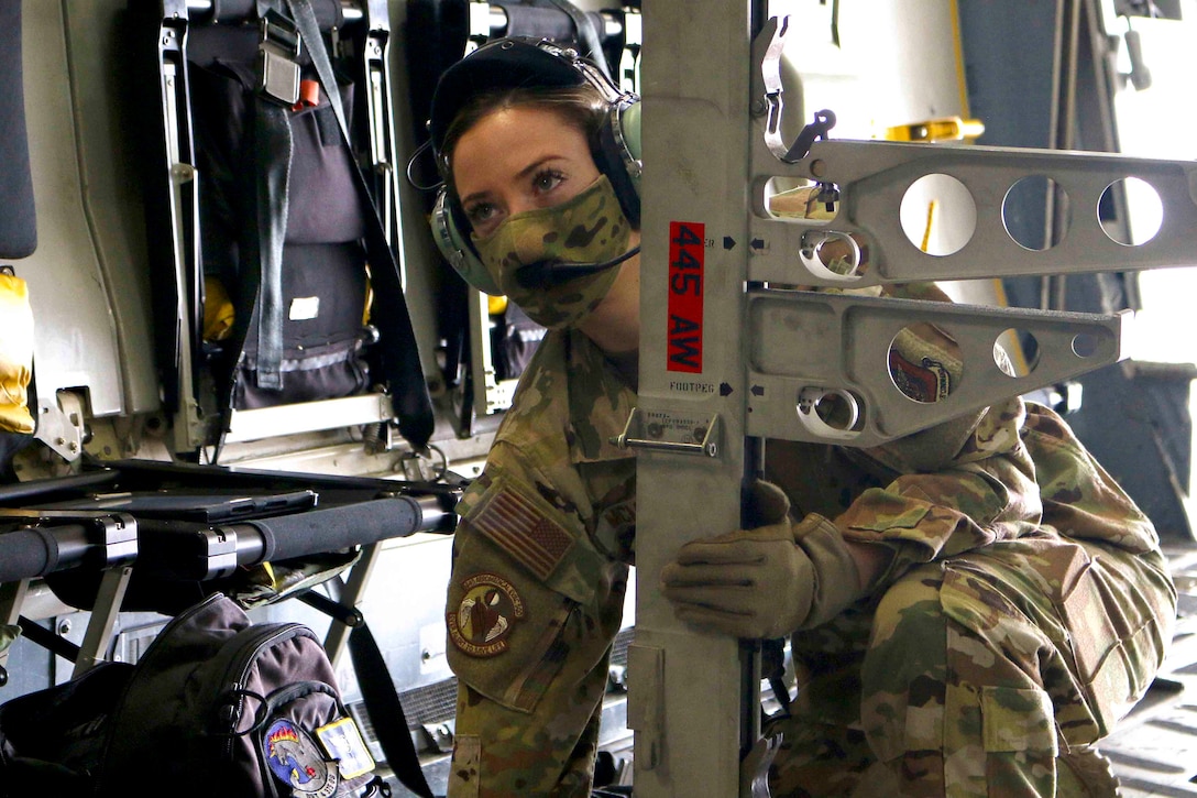 An airman kneels on the ground holding on to a metal pole.