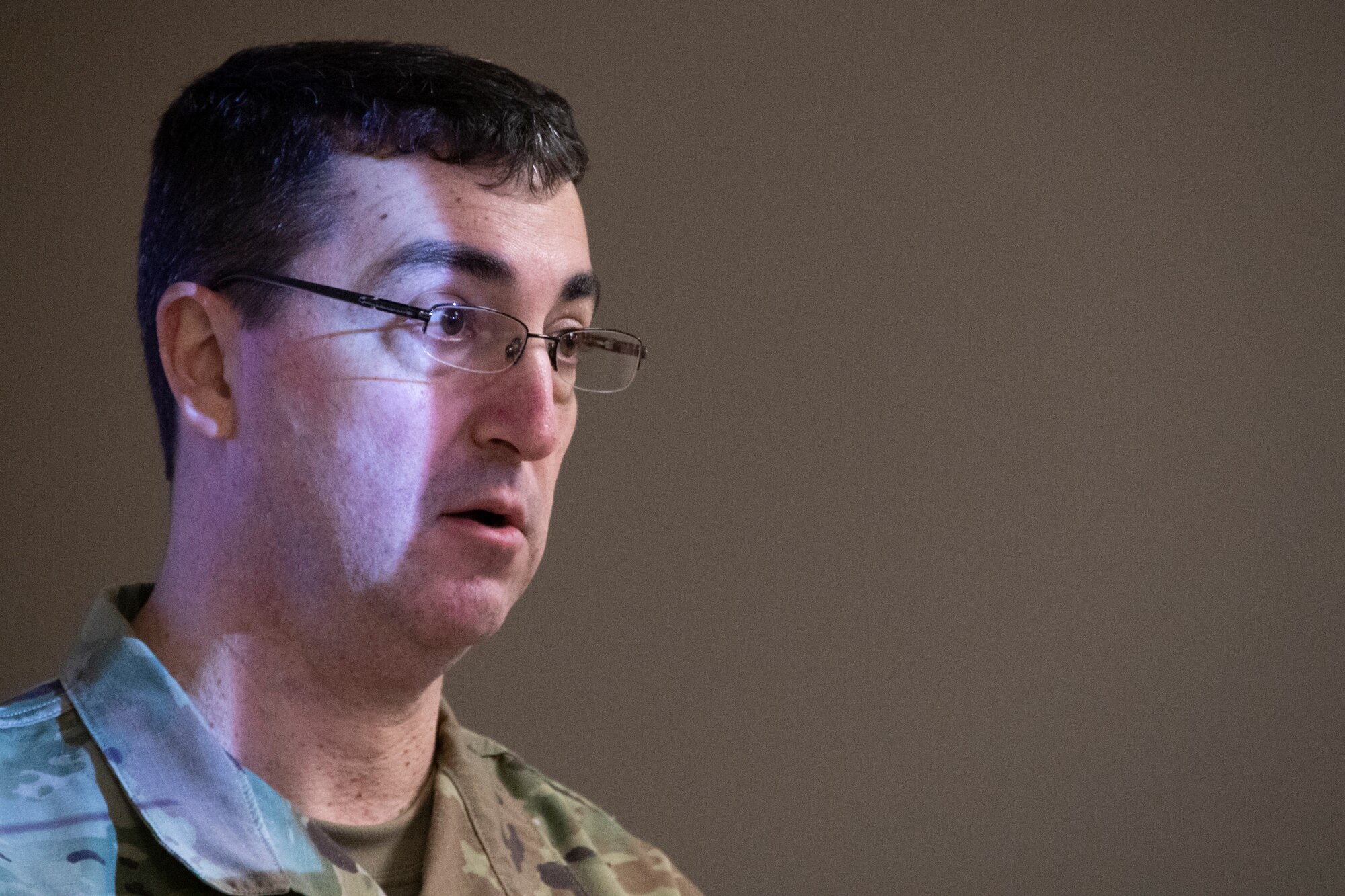 Close up shot of Airman giving a briefing. Light from the overhead projector reflects off his face.