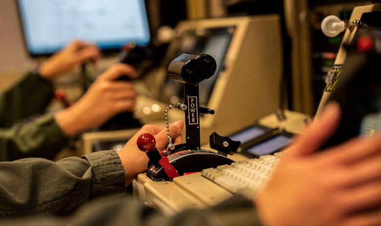An airman's hand rests beside simulator controls.