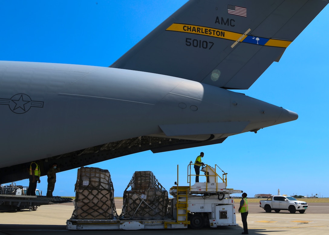 Two people stand on aircraft loading equipment, one above and one behind, ready to load the airplane from the rear. A view of the large rear section of a C-17 is in the shot as well.