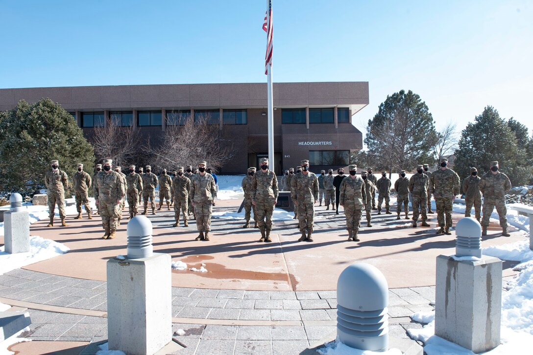 Group of Space Force personnel standing in formation outside around a flagpole.