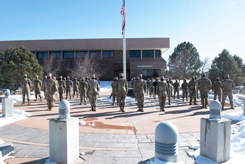 Group of Space Force personnel standing in formation outside around a flagpole.