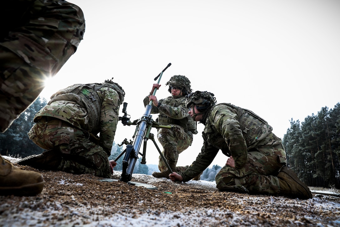 Paratroopers kneel on the ground and clean a weapon.