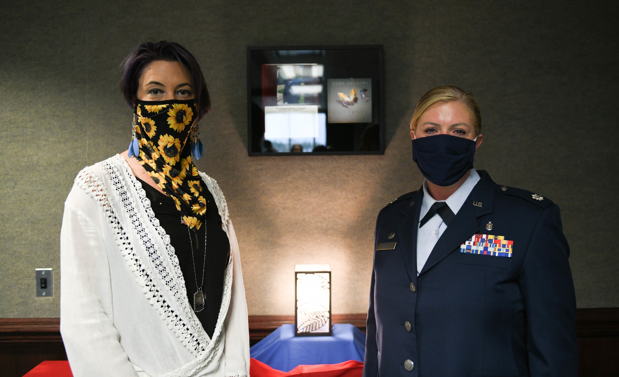 Two masked women stand next to each other in front of a plaque