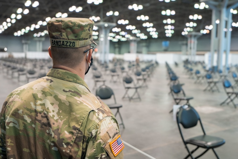 A soldier stands in a large room filled with chairs.