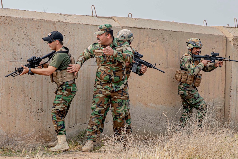 Four service members, three carrying weapons -- proceed around a bunker.