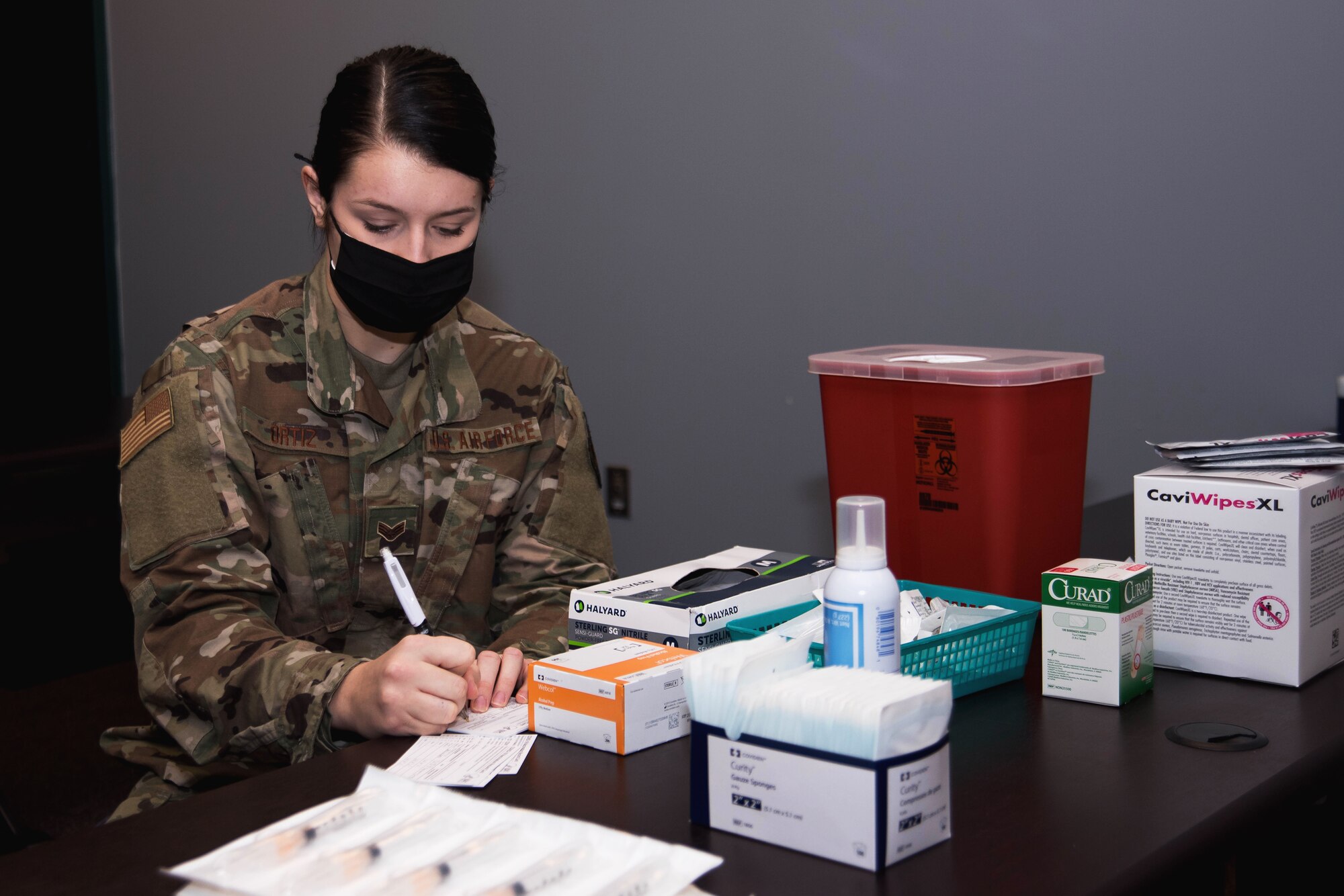 An Airman prepares COVID-19 vaccine paperwork while sitting at a table with medical supplies.