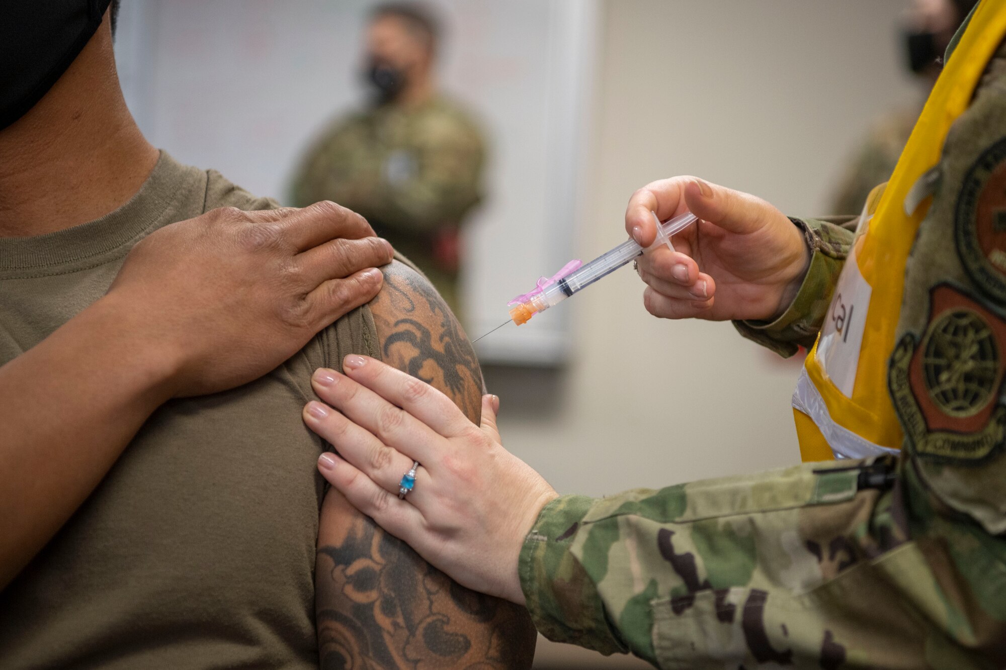 A medical technician issues a COVID-19 Vaccine to an airman's arm.