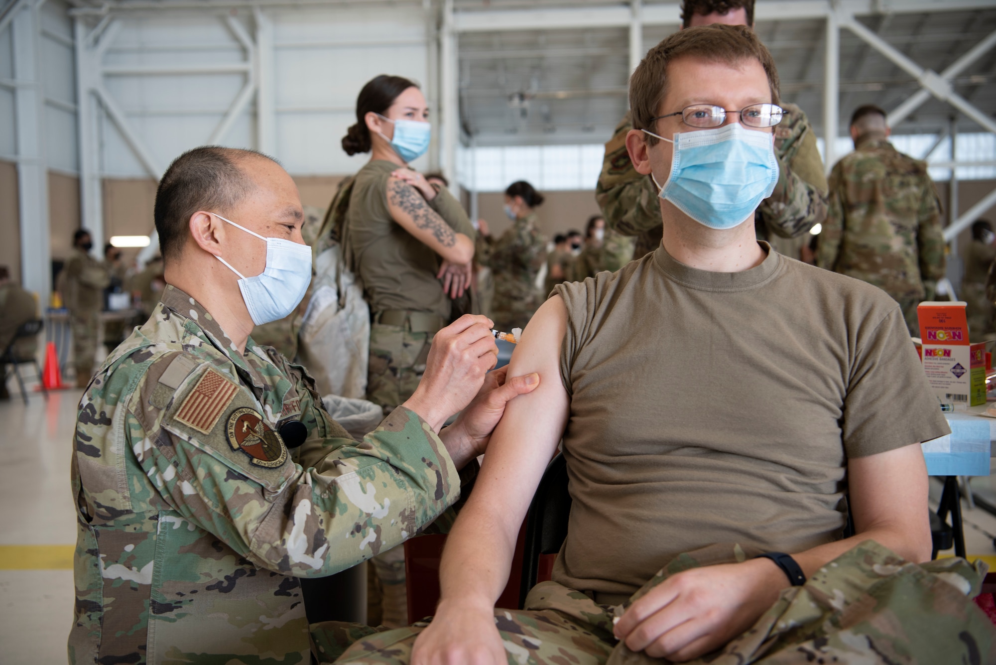 U.S. Air Force Maj. Jeffery Legaspi, 60th Surgical Operations Squadron operation nurse, injects Maj. Brett Mattison, 60th Medical Diagnostic and Therapeutic Squadron medical physicist, with the influenza vaccine at the point of distribution in a hangar Jan. 14, 2021, at Travis Air Force Base, California. The POD is an organized way of efficiently distributing a vaccine to a large amount of people and preparing medical personnel for future large-scale distributions such as the COVID-19 vaccine. (U.S. Air Force photo by Airman 1st Class Alexander Merchak)