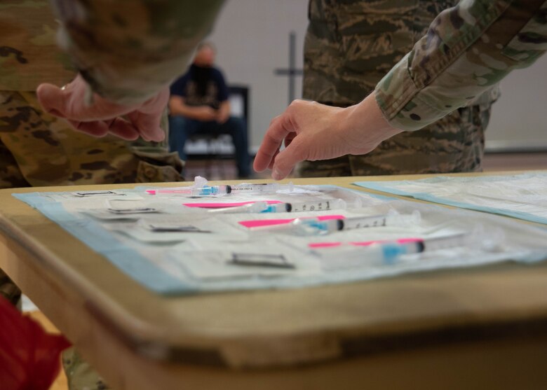 A military member placing syringes on a table.