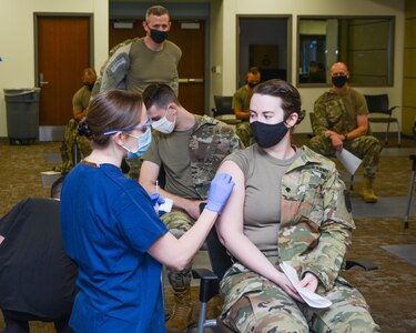 A female in an Army uniform receives a shot in her arm.