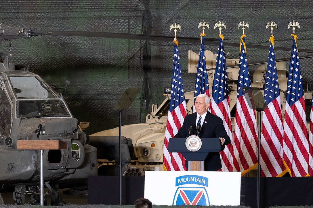 Man speaks to a hangar full of soldiers.