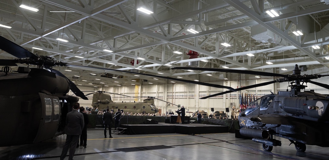 A man stands at a podium with helicopters and flags behind him.