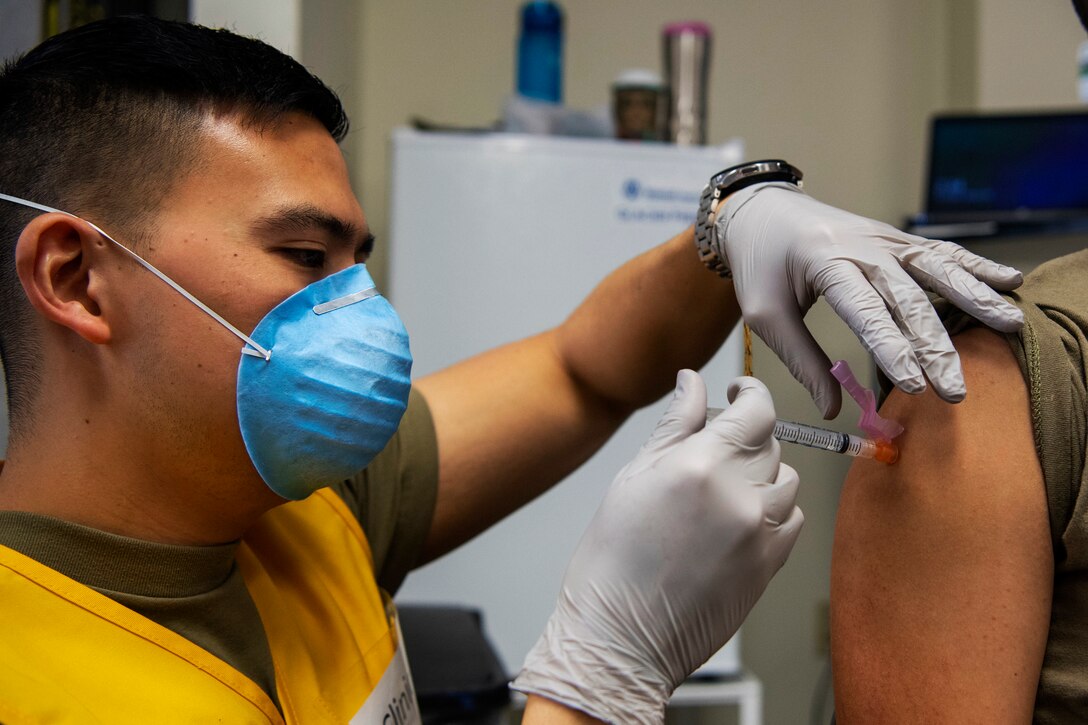 An airman wearing a face mask and gloves gives a vaccine to someone.