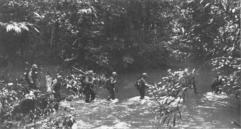 An historic photograph from 1943 shows Marines crossing a stream.