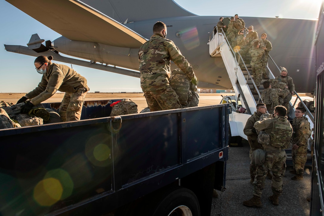 Airmen and soldiers load bags onto a plane from a truck.