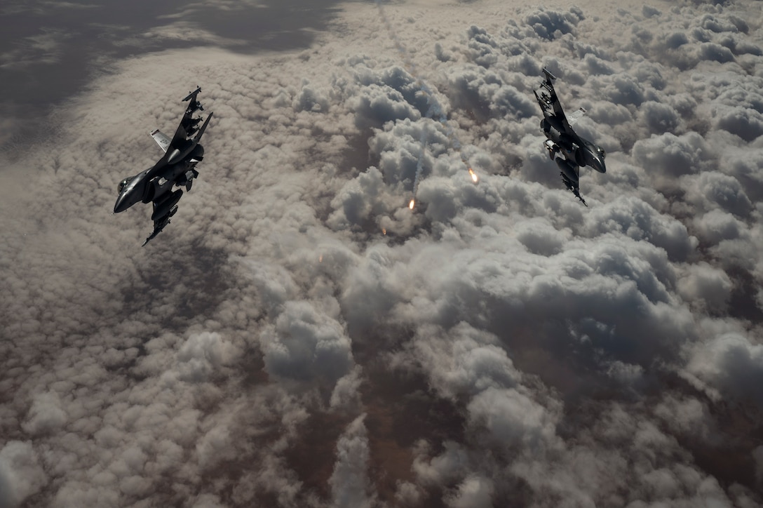 Two aircraft fly above the clouds and release flares.