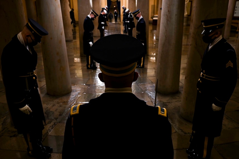 In an indoor setting, service members stand in formation amid columns.