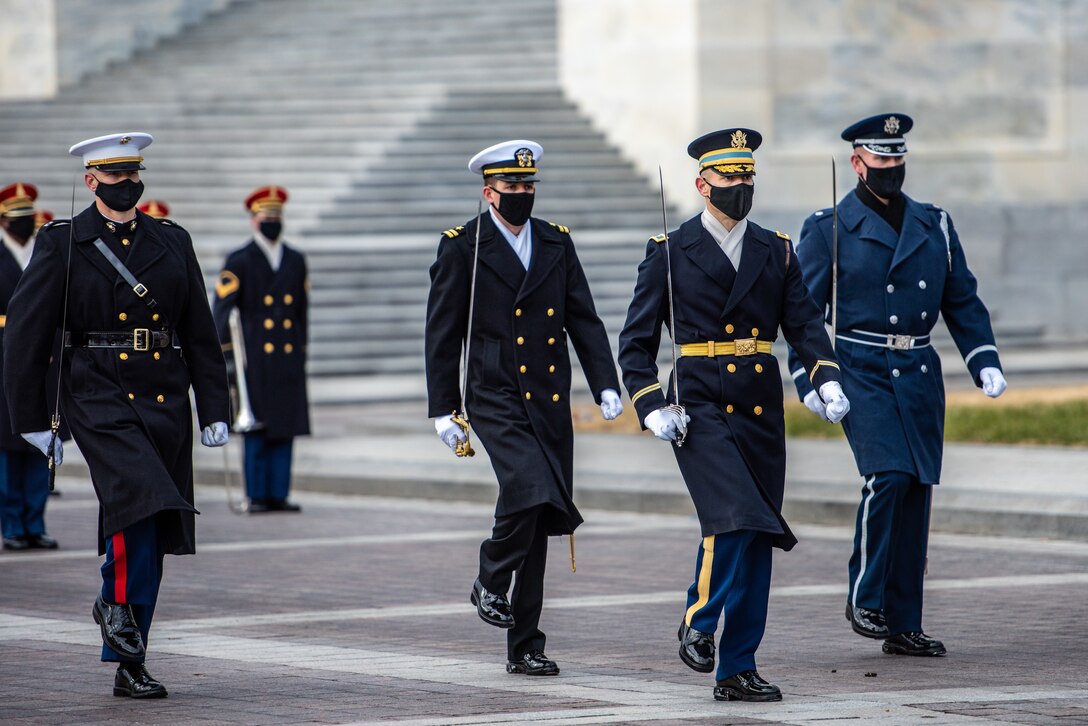Service members march while carrying sabers.