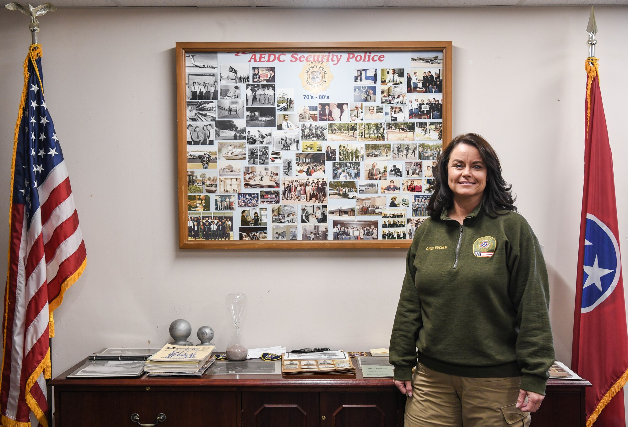 Regina Bucher, the new Security Services Supervisor at Arnold Air Force Base, Tenn., stands in front of a collage of photos showing security services personnel over the years in her office Dec. 8, 2020. She is the first female to lead the contractor security section. (U.S. Air Force photo by Jill Pickett)