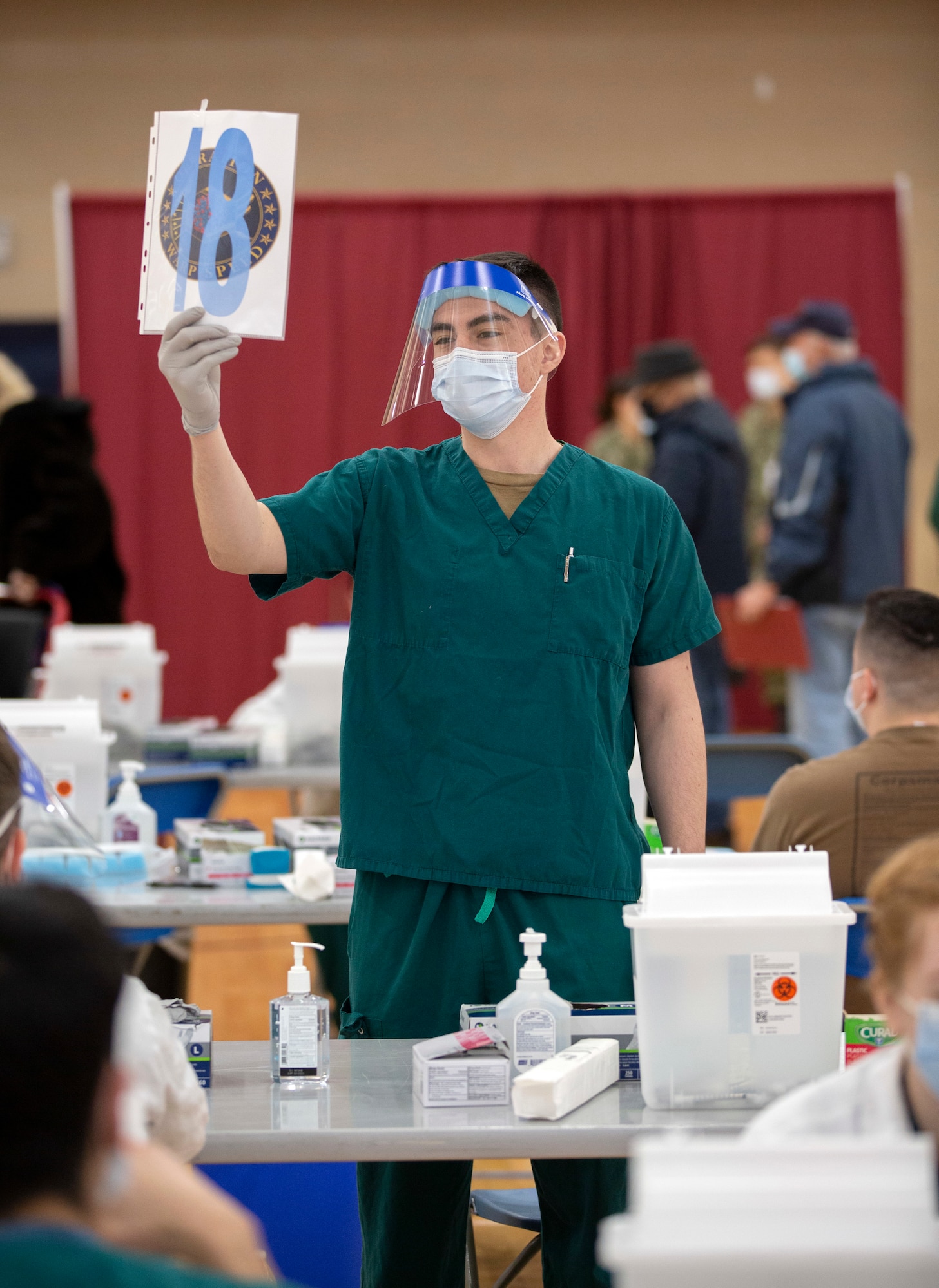 Hospital Corpsman 3rd Class Charles Cambern holds up a numbered sign as patients circle through to receive the COVID-19 vaccine as part of Operation Warp Speed at Walter Reed National Military Medical Center.