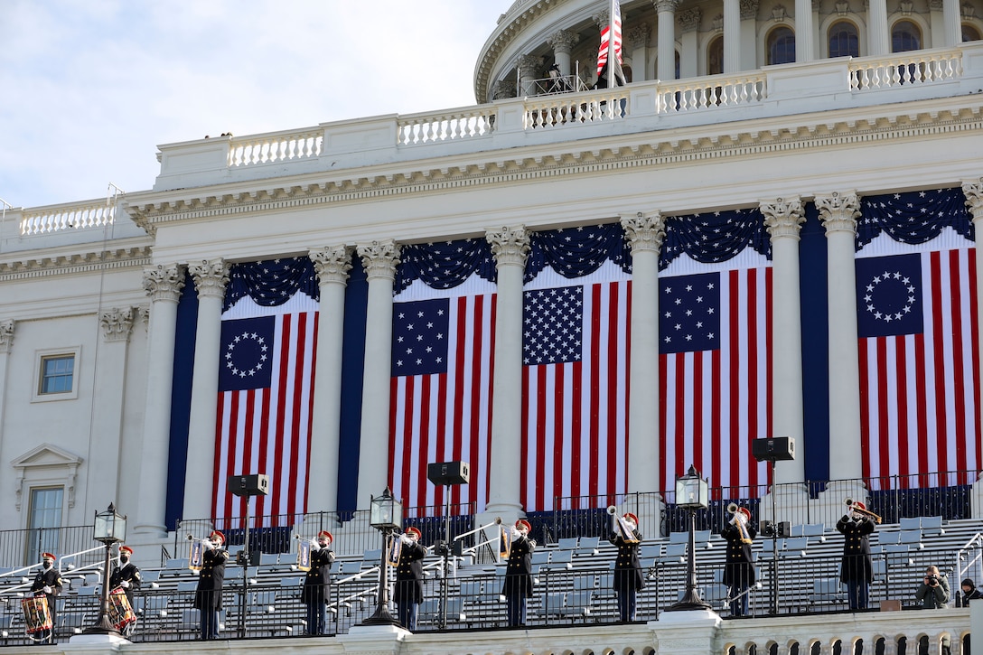 A row of people in uniform play trumpets on the steps of the Capitol Building in Washington, D.C.