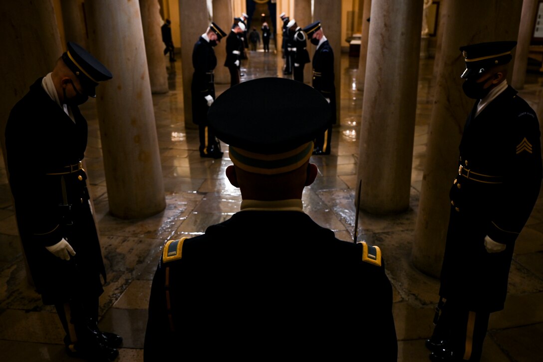 Service members stand in a formation in a darkened hallway.