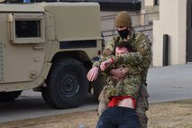 An Airman grips an injured Airman around the chest and drags him backwards behind a Humvee for cover during a simulated training exercise.
