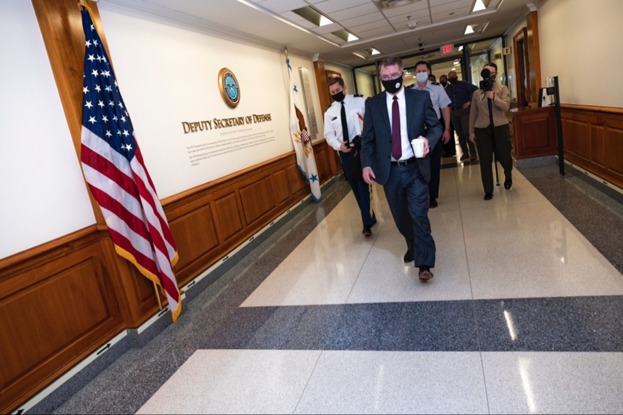 A man walks down a hall carrying a cup as others follow.