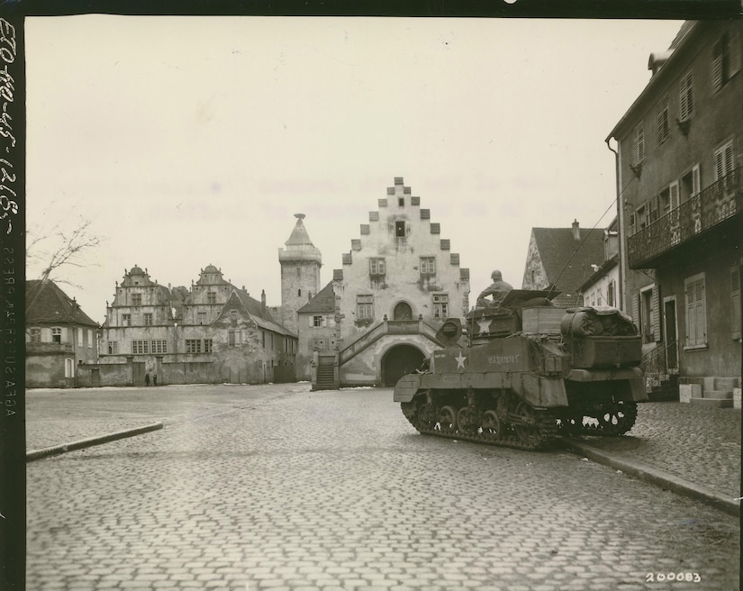 A historic photo shows a tank parked on the road and sidewalk of a deserted town.