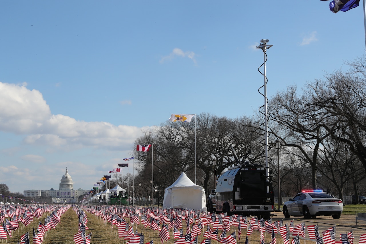 A tactical command vehicle parks near the U.S. Capitol beside a field of American flags.