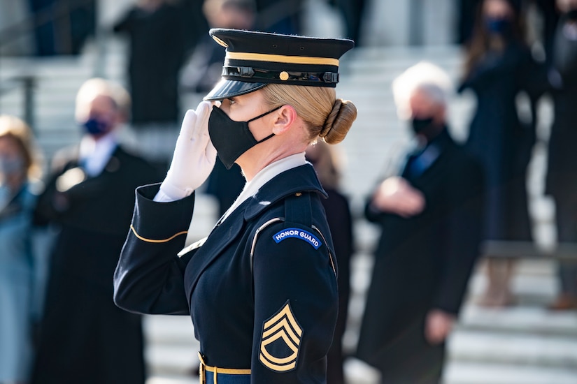 A soldier salutes at an outdoor ceremony.