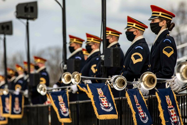 Band members stand in a line while carrying trumpets.