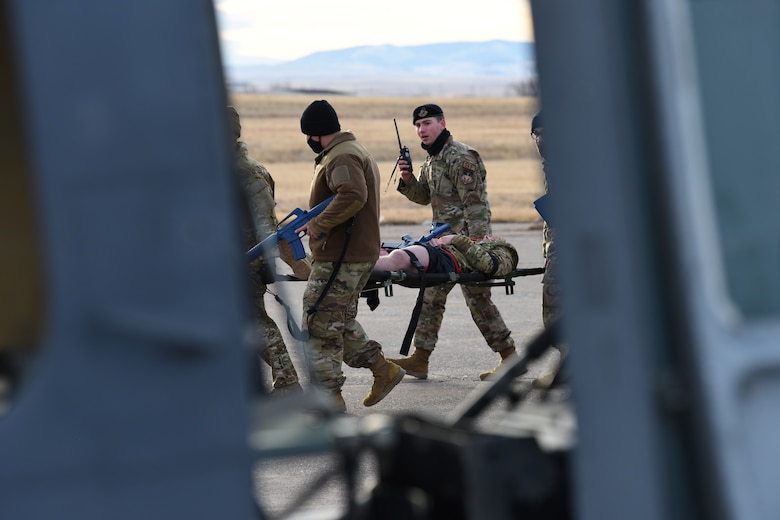 Convoy team members are escorting an injured Airmen on a stretcher towards a helicopter for evacuation.