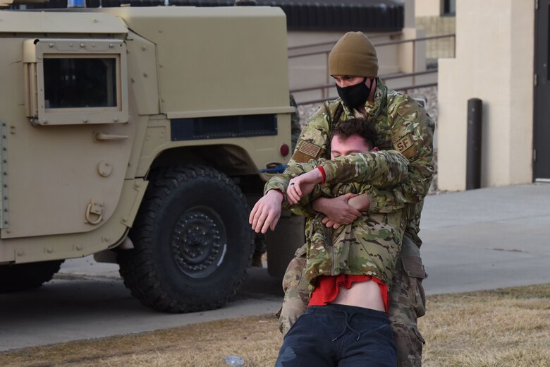 An Airman grips an injured Airman around the chest and drags him backwards behind a Humvee for cover during a simulated training exercise.