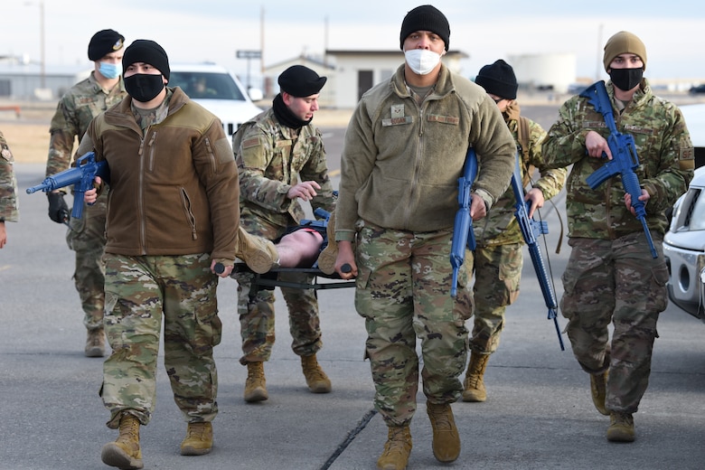 Convoy members escort an injured Airmen on a stretcher and are on high alert for other unidentified explosive devices during a training exercise.