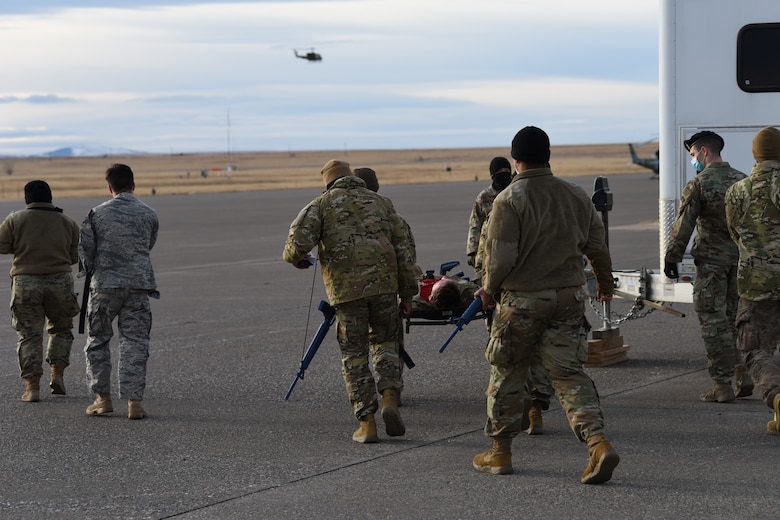 Convoy members escort an injured Airman towards a helicopter for evacuation.