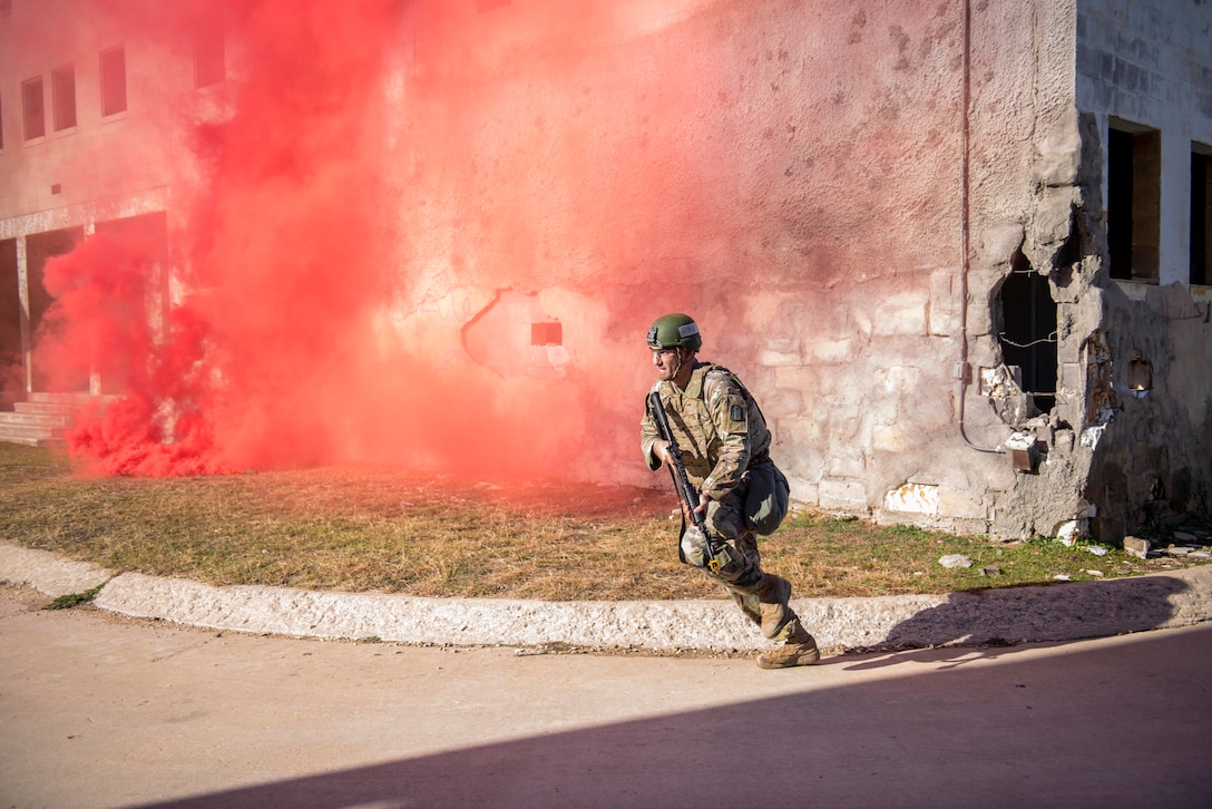 A soldiers runs while carrying a weapon near a cloud of red smoke.