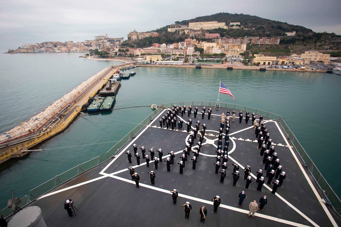 A large group of sailors stand in formation on the deck of a ship.