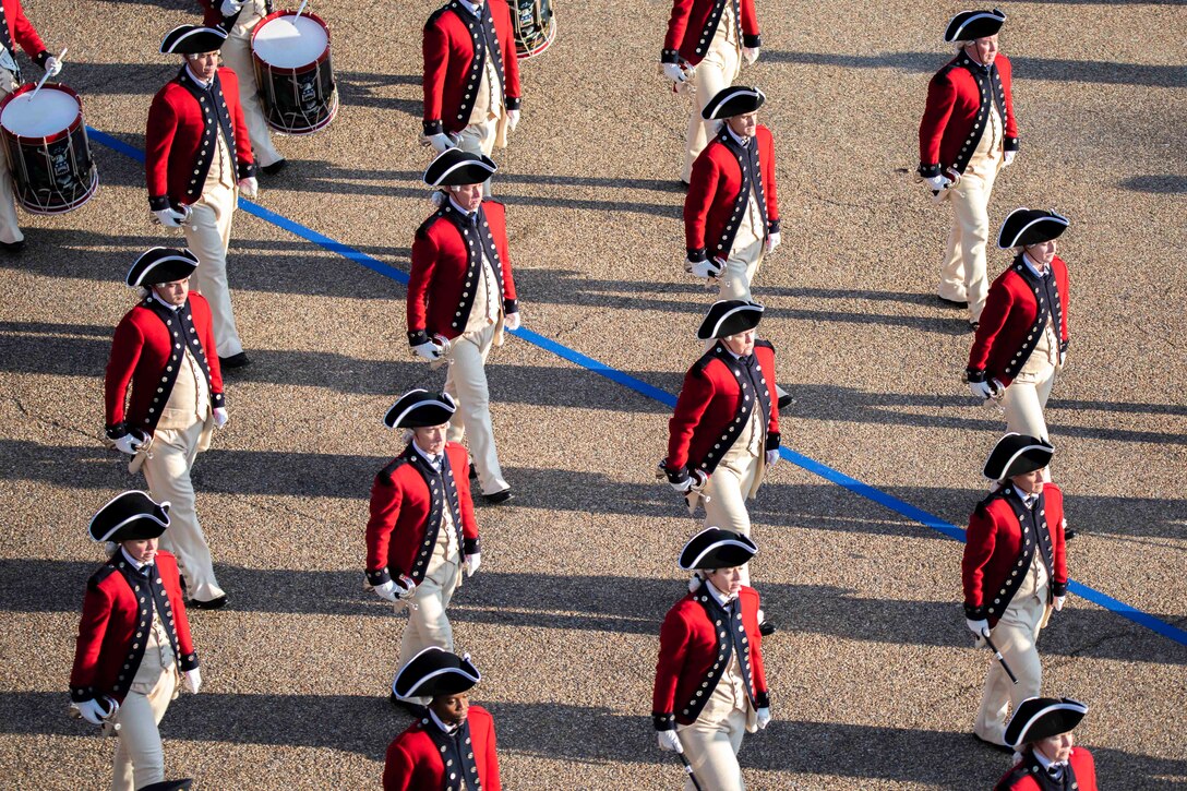 A group of soldiers walk in formation; some hold drums.