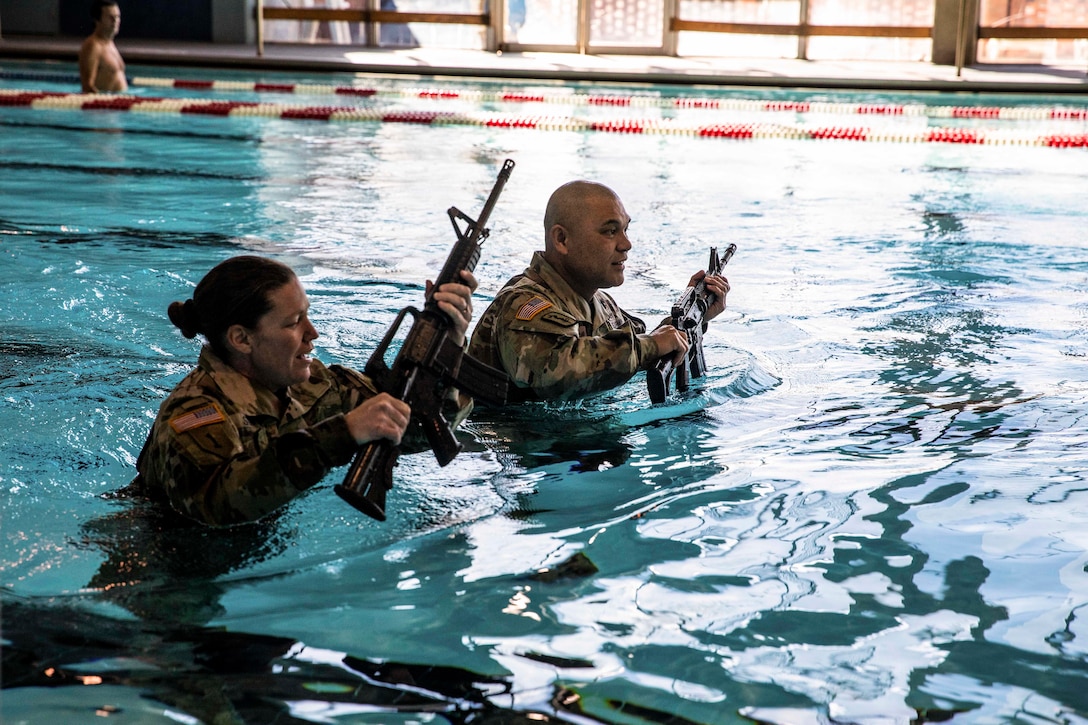 Soldiers carry weapons as they move across a pool.