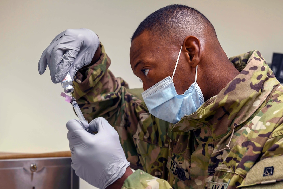 A soldier wearing a face mask and gloves fills a syringe with a dose of  COVID-19 vaccine.