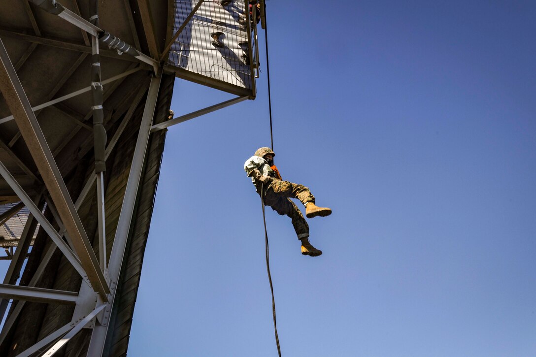 A Marine Corps recruit rappels down a tower.