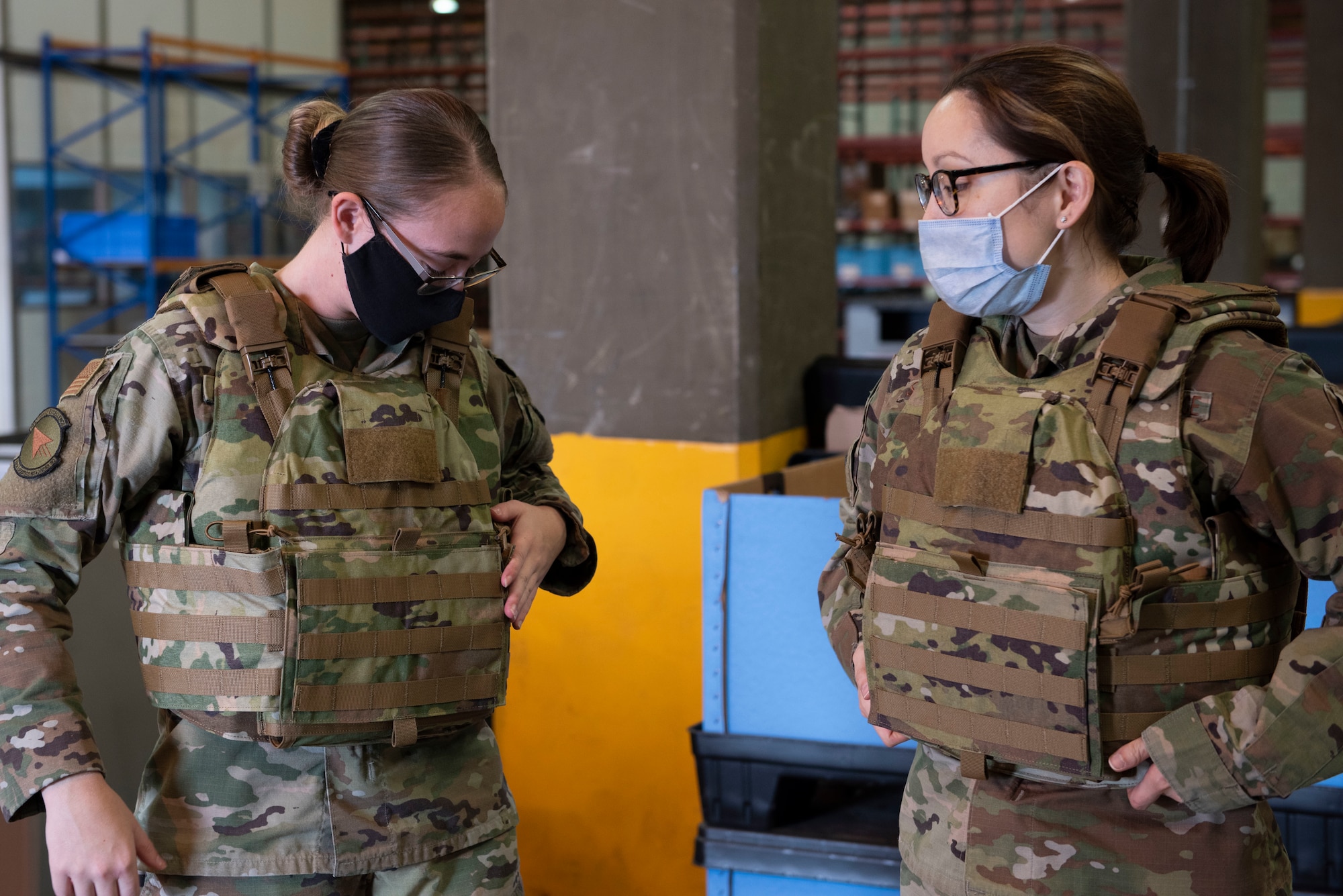 Two Airmen women try on body armor vests together.