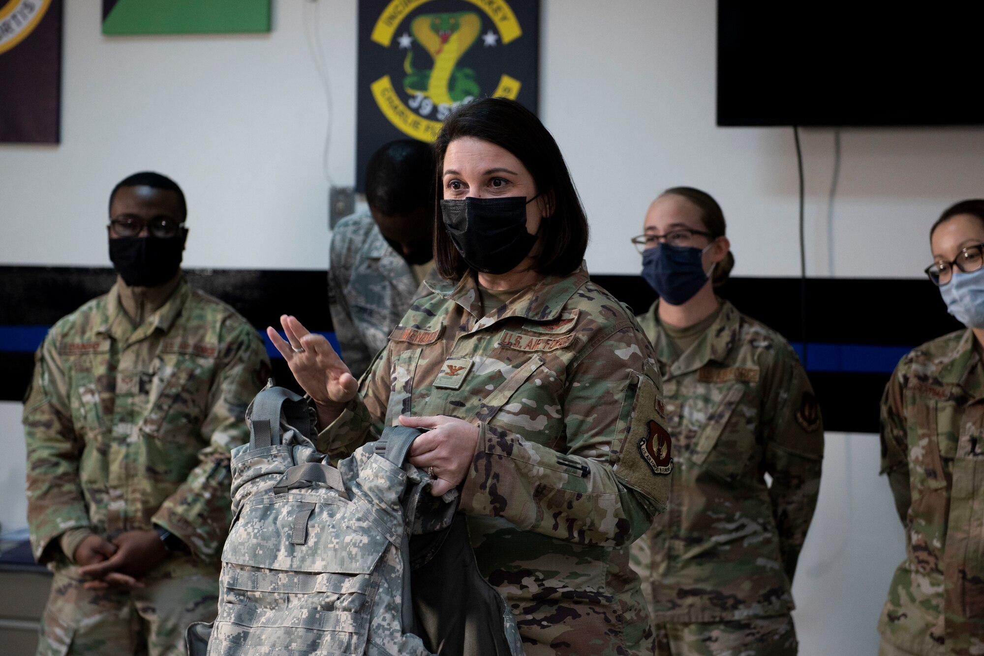 A female colonel holding up an armored vest while speaking to a small crowd
