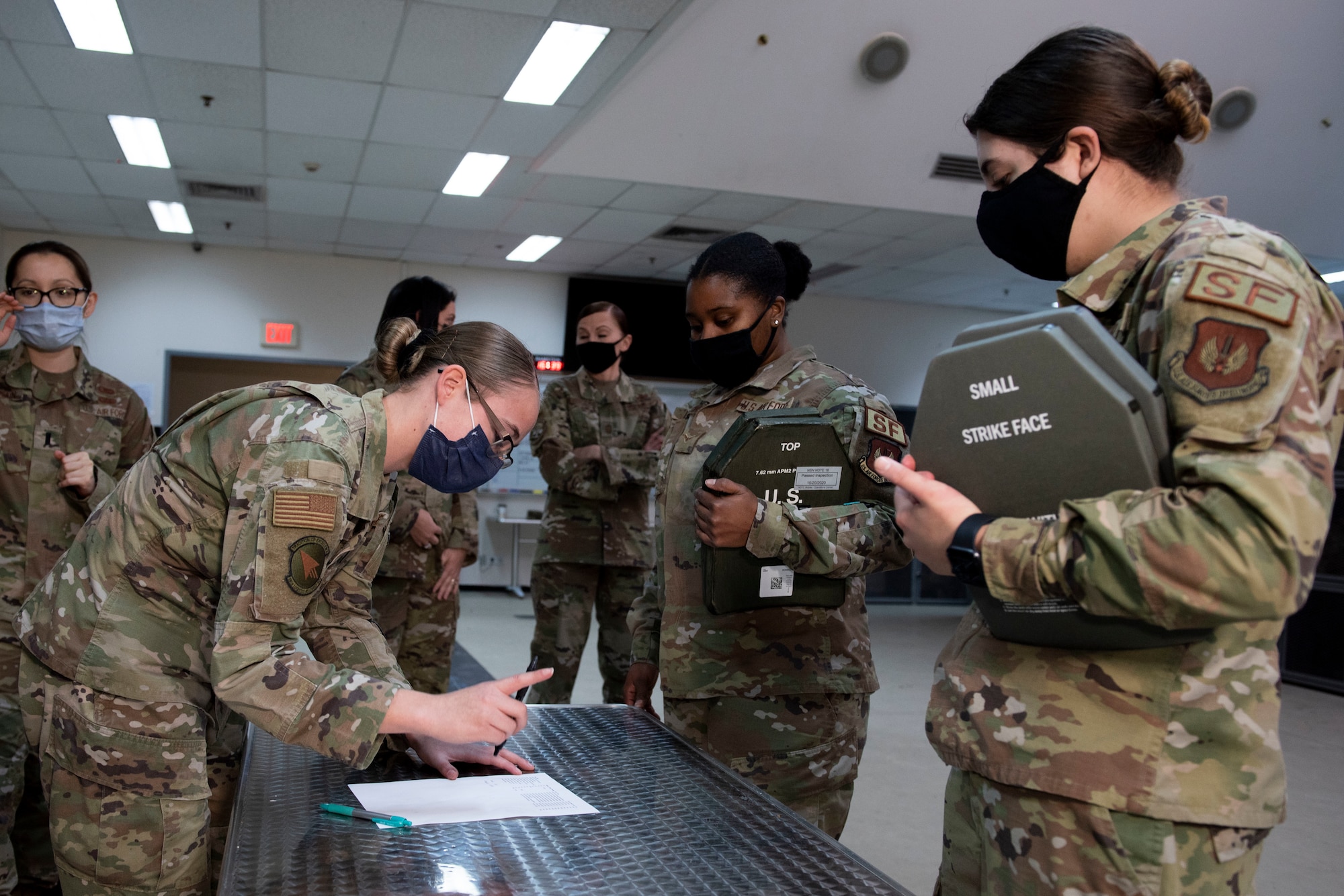 Women security forces Airmen line-up at a table to be issued new armored vests.