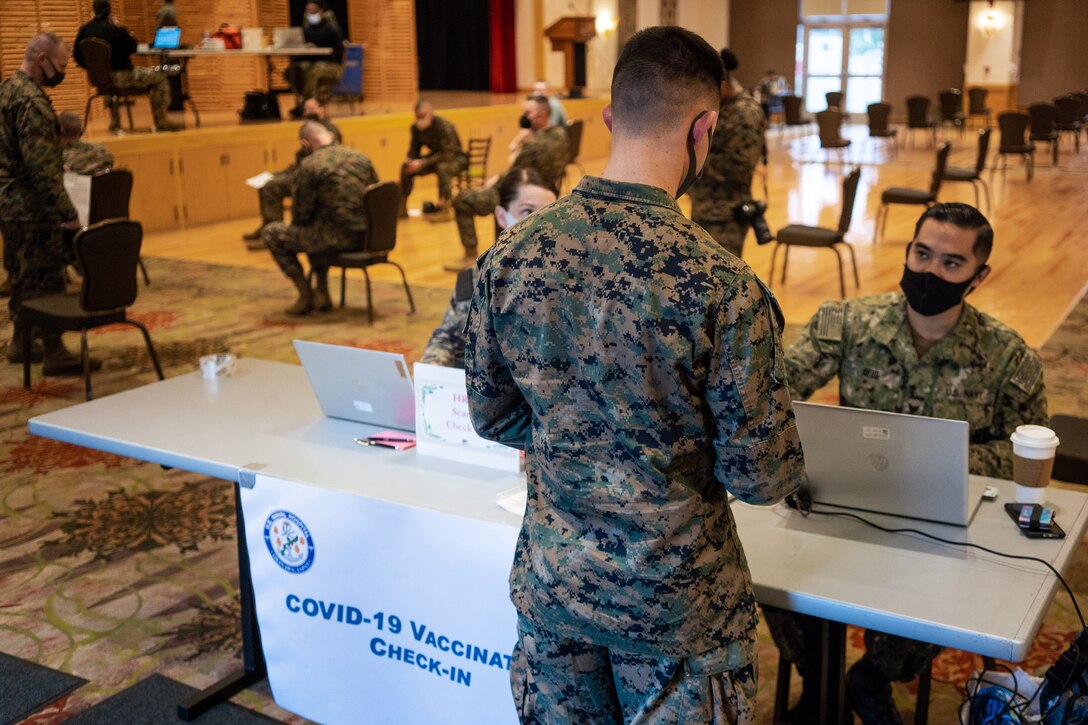 A Marine stands at a table to check in for his COVID-19 vaccination.