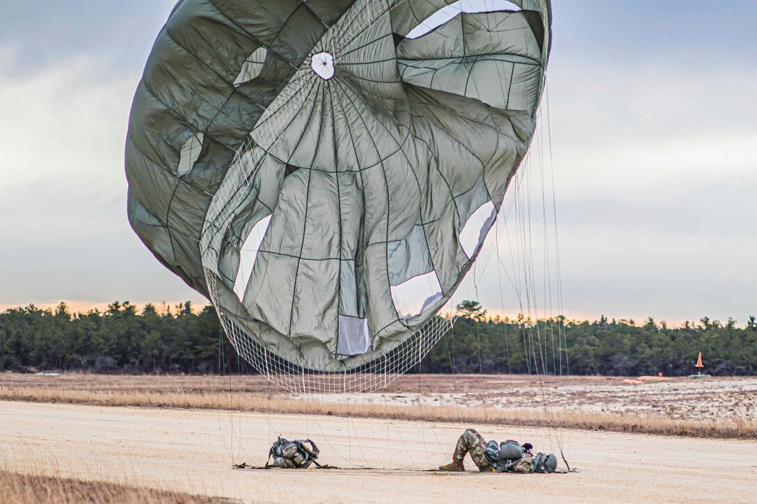 A soldier lies on the ground wearing an open parachute.