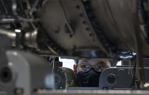 A photo of an Airman looking under an engine.